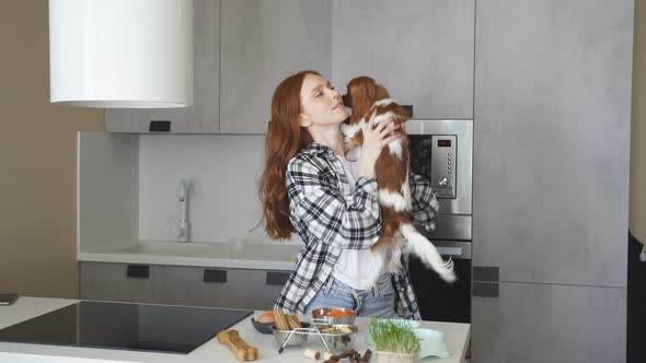 Redhaired Woman Feeds Holds Her Dog in Her Arms in the Kitchen She Loves and Hugs Her Spaniel Dog