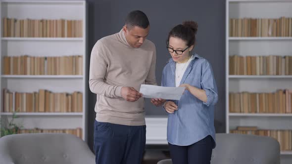 Positive Young African American Man and Caucasian Woman Giving Highfive Standing in Living Room alt