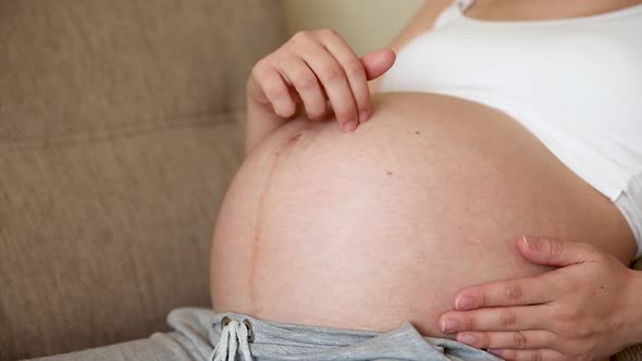 A Caring Mother Strokes a Naked Pregnant Tummy with Two Hands on Light Room alt