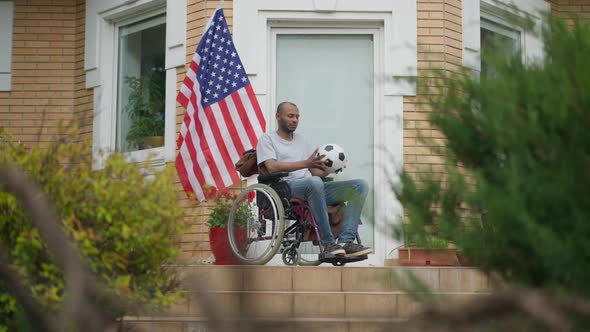 Frustrated African American Disabled Man Sitting in Wheelchair Holding Soccer Ball alt