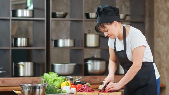 Smiling Female Chef Cuts Fresh Meat on Table Preparing Food alt
