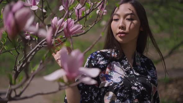 Young Asian Woman in Kimono Walking in Slow Motion in Sakura Garden Touching Pink Flowers on Tree alt