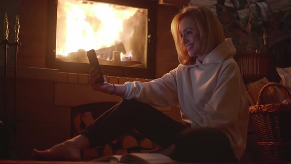 An European Young Woman Having Video Call Near Fireplace alt