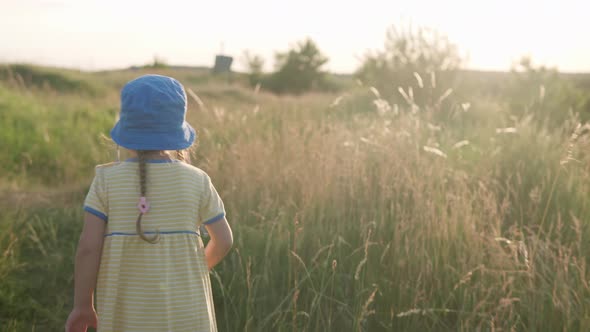 Cute Preschool Little Baby Girl in Yellow Dress Climbing Up Trail in Tall Grass Before Sunset alt