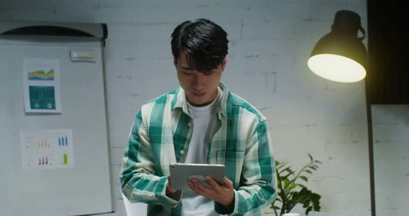 Young Asian Man Smiling Looking at Camera While Standing with Tablet in Office alt