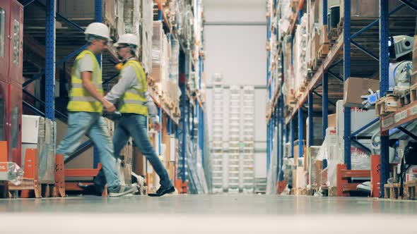 Warehouse Workers and Robot Moving Along the Aisle alt