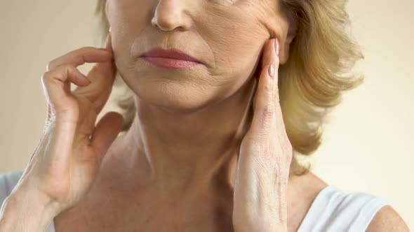 Woman Pulling Sagging Skin on Face With Fingers, Thinking About Plastic Surgery alt