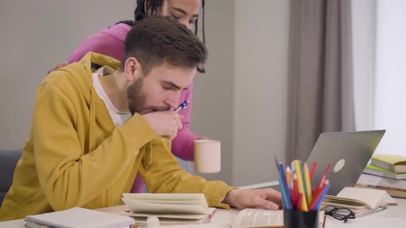 Attractive African American Girl Bringing Cup of Tea or Coffee for Young Caucasian Boy Sitting at alt