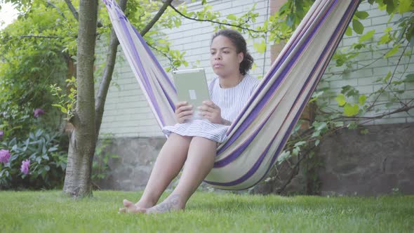 Portrait Cute Young African American Woman Sitting in the Hammock, Relaxing in the Garden, Texting alt