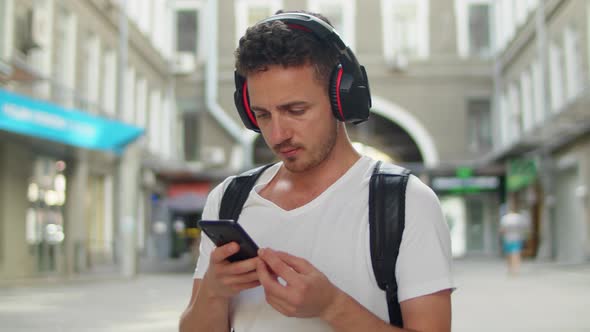 Smiling and Laughing Handsome Young Man Listening Music From His Smartphone in Red Headphones on alt