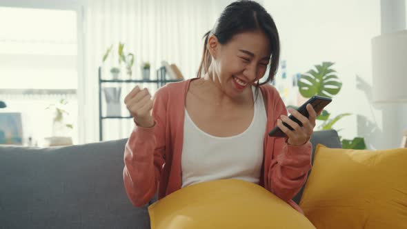 Beautiful asian lady sitting on sofa feel exciting with great news at home alt