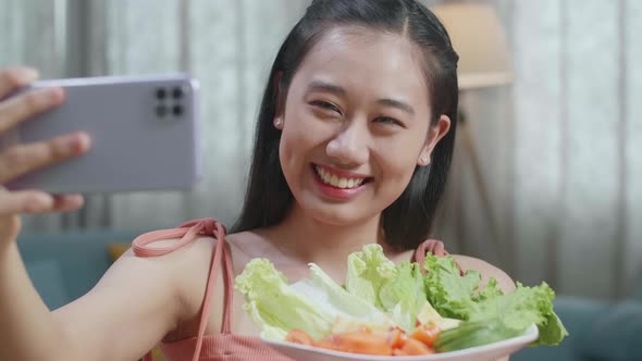 Close Up Of Asian Woman Holding A Dish Of Healthy Food And Taking Selfie With Smartphone At Home alt