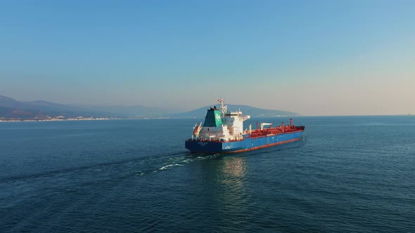 Aerial View Following the Ultra Large Cargo Ship at Sea Leaves Port at Sunny Day alt