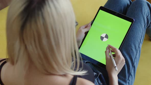 Female Artist is Sitting Sofa and Drawing with Stylus on Tablet with Chromakey Screen Back View alt