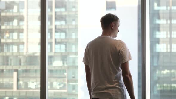 Rear View of a Business Man Standing By the Window in Office Looking Out at Modern Buildings
