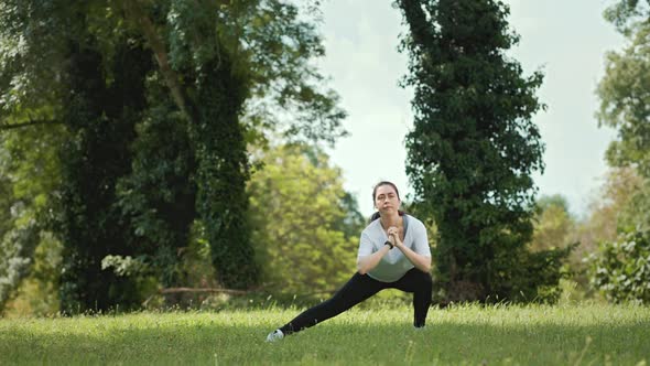 Outdoors warmup. A young pretty woman performs warm-up squats in the park. alt