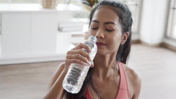 Attractive Asian female in sportswear drinking water after doing exercise yoga workout.