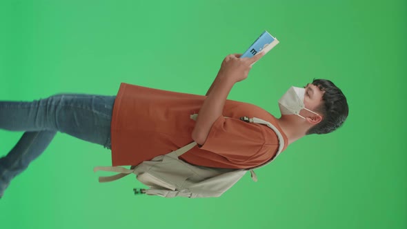Asian Boy Student Wearing A Mask, Reading A Book While Walking To School On Green Screen alt