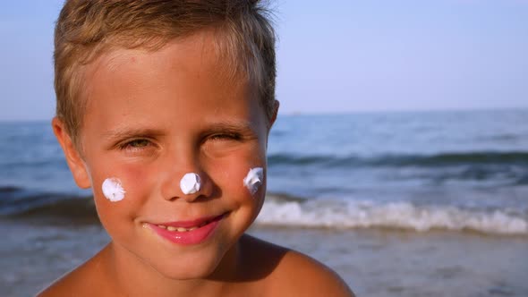 Cute Boy with Sunscreen on His Face Against the Backdrop of the Sea alt