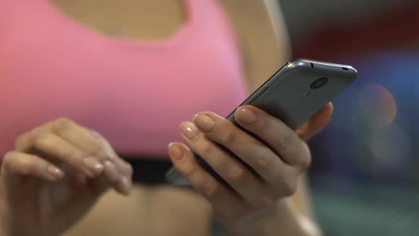 Active woman scrolling screen of smartphone in gym, using sports mobile app alt