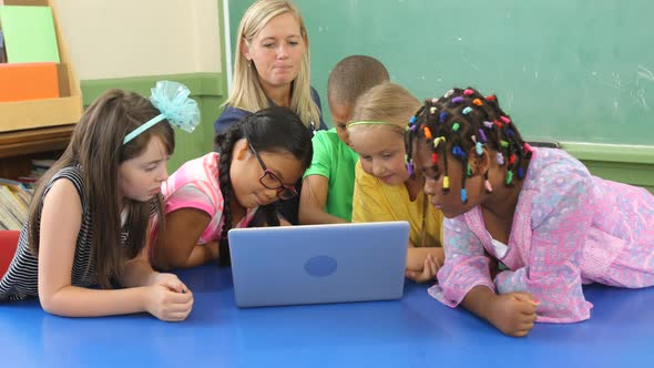 Teacher and students work on laptop computer in school classroom alt