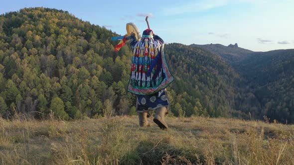 Energetic Dance of an Old Shaman with a Tambourine on the Background of Autumn Mountain Landscape