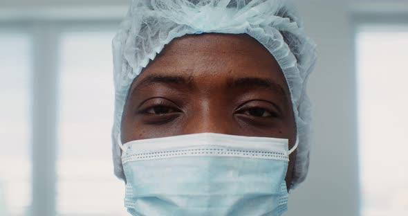 A Young AfricanAmerican Doctor with Medical Cap and Mask Looks Into Camera alt