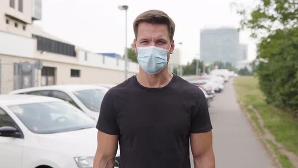 A Young Handsome Man in a Face Mask Talks To the Camera in a Parking Lot in an Urban Area alt