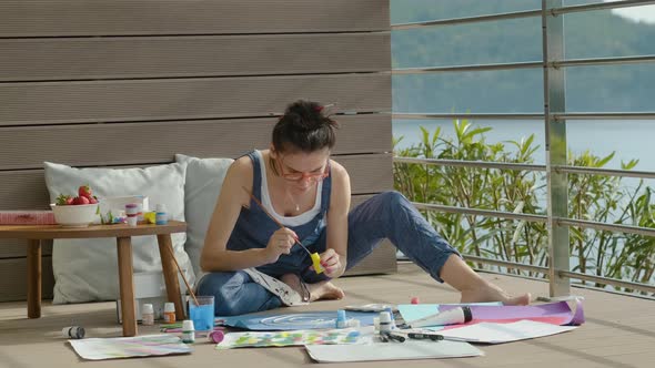 Young American Woman is Engaged in Creativity Using Paints While Sitting at Home Terrace Rbbro alt