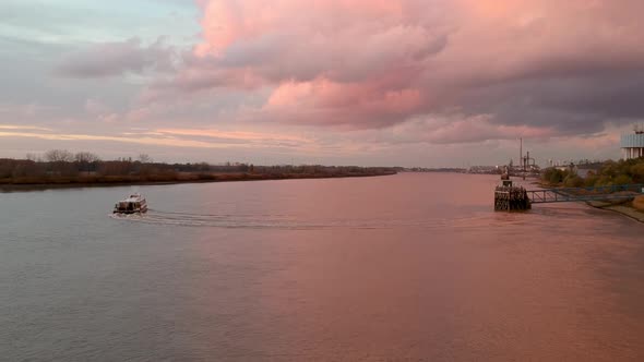 Drone captures a boat sailing away under pink light reflecting off the river and clouds. alt
