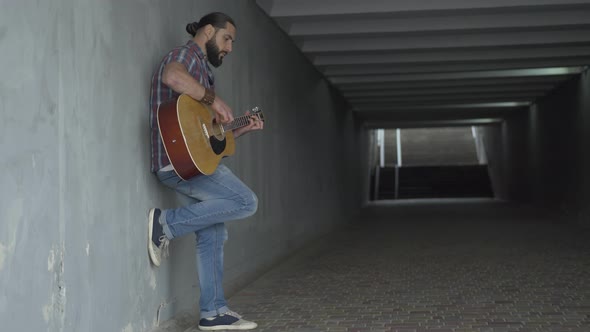 Side View Wide Shot of Engrossed Caucasian Guitarist Playing in Underground Crossing. Absorbed Man alt