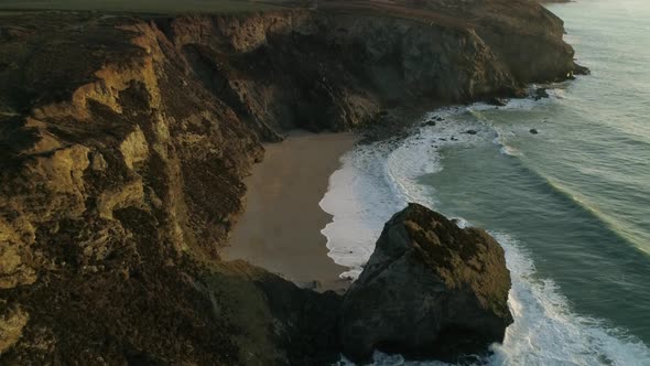Cinematic slow motion aerial shot of waves at sunset along cornish coastline alt