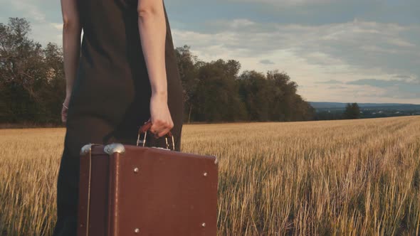 Female Carrying A Suitcase In A Field