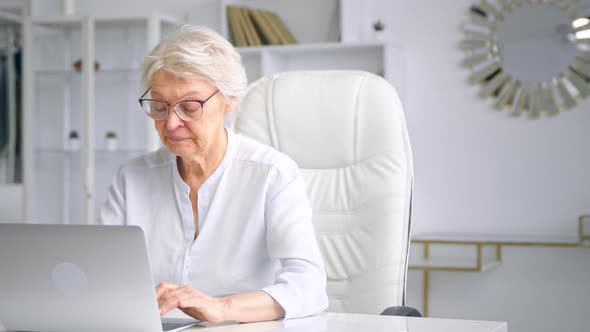 Concentrated aged lady manager in glasses types on grey laptop keyboard alt