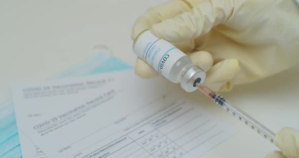 Close Up of Hand Filling a Syringe with Liquid From a Vial with a Label Reading Covid19 Vaccine alt