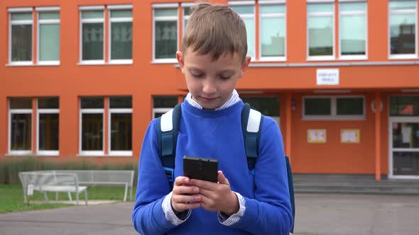 A Young Boy Works on a Smartphone, Then Looks at the Camera and Smiles - an Elementary School alt