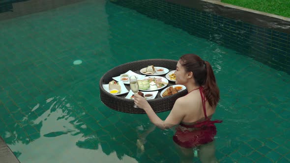 cheerful young woman enjoying with floating food and champagne glass in swimming pool