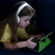 Cute small kid girl in headphones using tablet lying on sofa