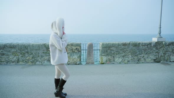 Woman Walks on Embankment with Stone Fence Against Lake alt