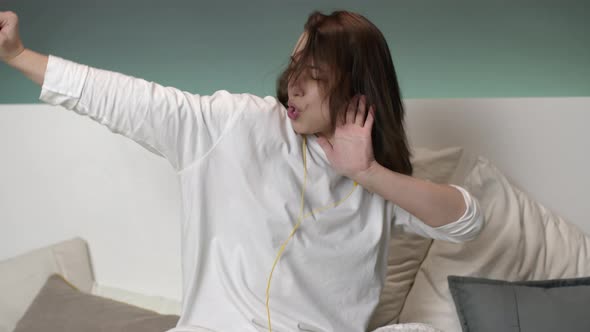 Young Attractive Happy Woman with Yellow Headphones Listening To Music on Bed alt