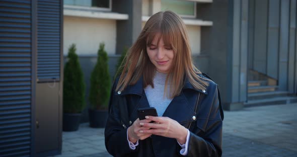 Portrait of Happy Blonde Hipster Woman Typing By Mobile Phone Outdoors alt