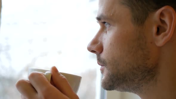 Closeup of a Young Man Standing in His Kitchen Drinking Coffee From a White Cup