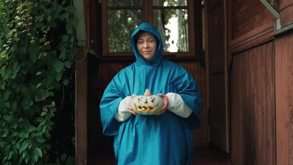 Woman in a Raincoat with a Pumpkin for Halloween on the Porch of an Old House