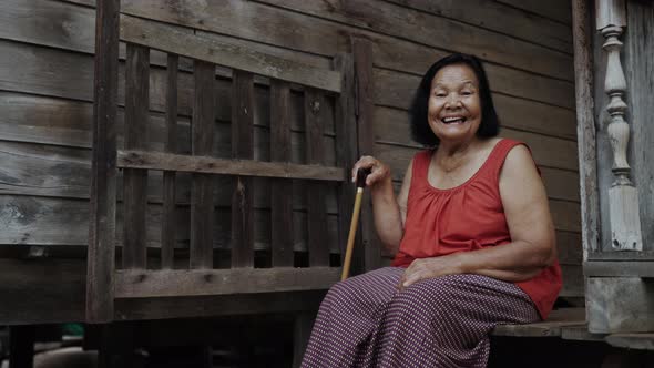 Thai elderly woman in round-necked sleeveless collar laughing in old wooden home alt