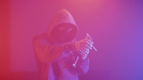 man in a balaclava in a dark room talking on a smartphone alt