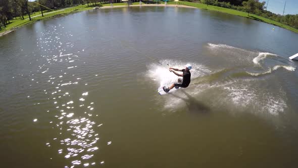 Aerial drone shot of a man riding his wakeboard at a cable park. alt