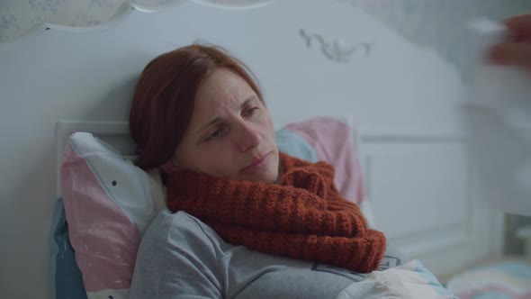 Sick Young Woman Laying in Bed. Woman with Warm Scarf on Neck Coughs. Hand with Napkin Appears and alt