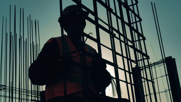 Man in Uniform Knits Reinforcement Bars on Construction Site. alt