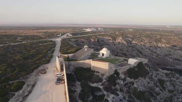 Drone hovering toward cliffside fortress and chapel - Fort of Santo António de Belixe Sagres alt