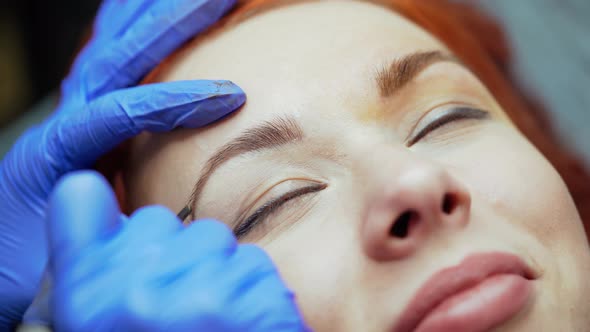 Hands of the Master are Putting a Tattoo on the Edge of the Eyebrow  alt